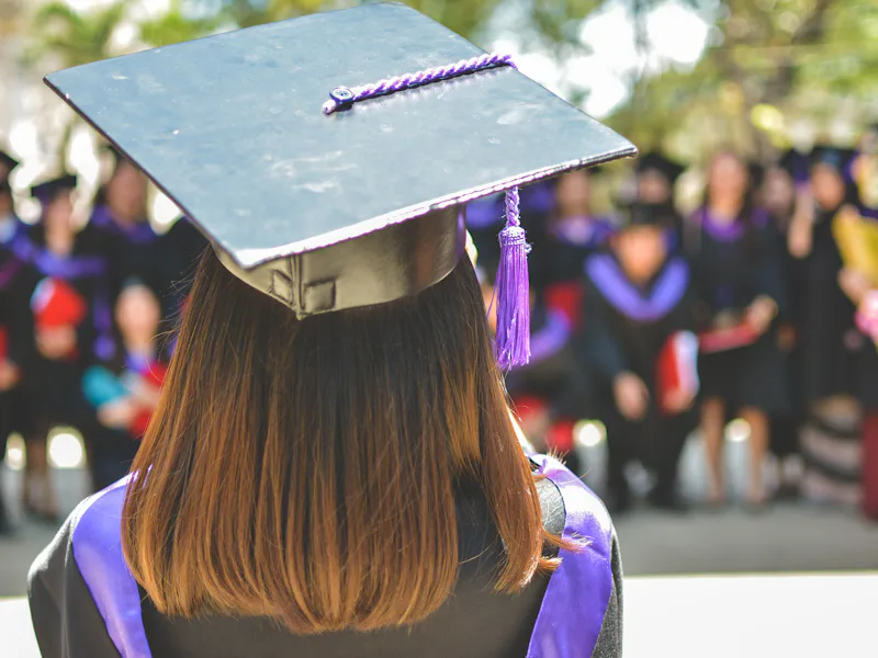 A graduate in a cap and gown facing a ceremony