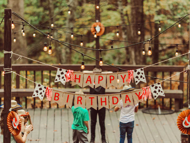 Children at an outdoor birthday party under a banner and string lights
