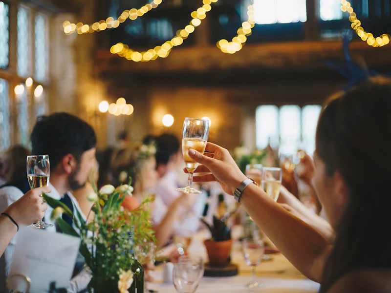 Guests raising glasses at a long dinner table with string lights