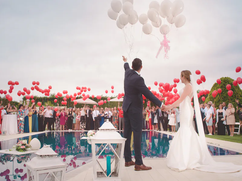 A couple releasing balloons beside a pool while guests watch